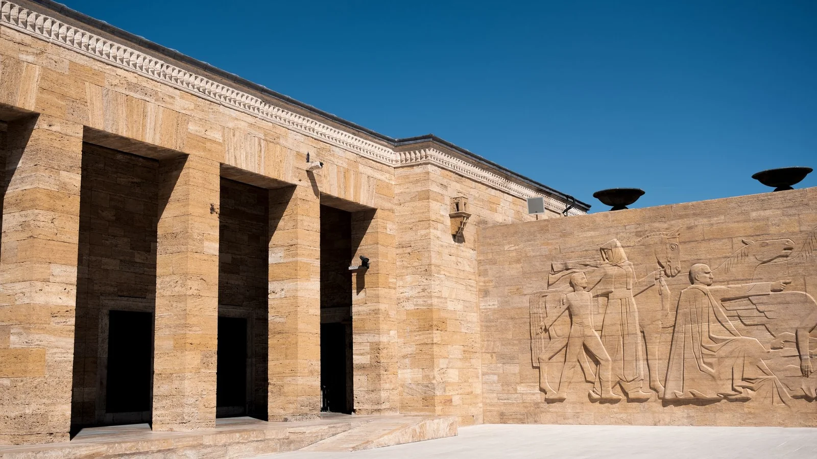 Stone colonnades and a large carved relief at Anıtkabir under a clear blue sky.