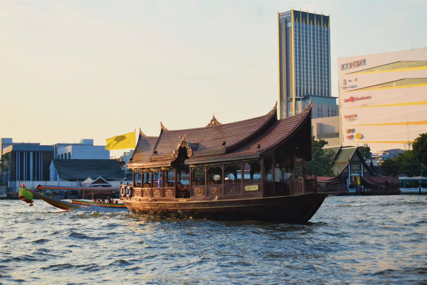 Traditional Thai boat moving along Bangkok’s Chao Phraya River at dusk.