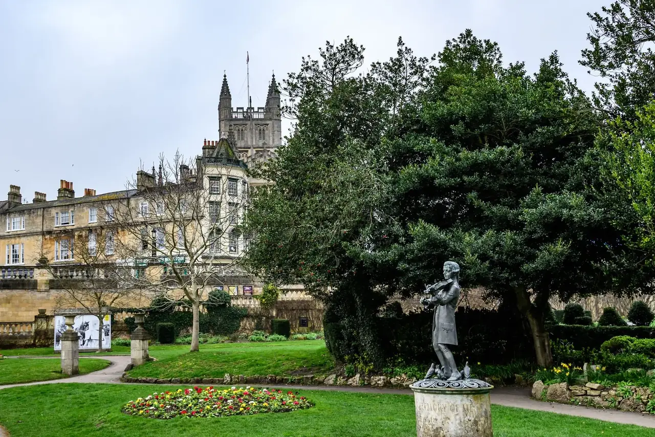 A statue and historic architecture in a landscaped Bath park