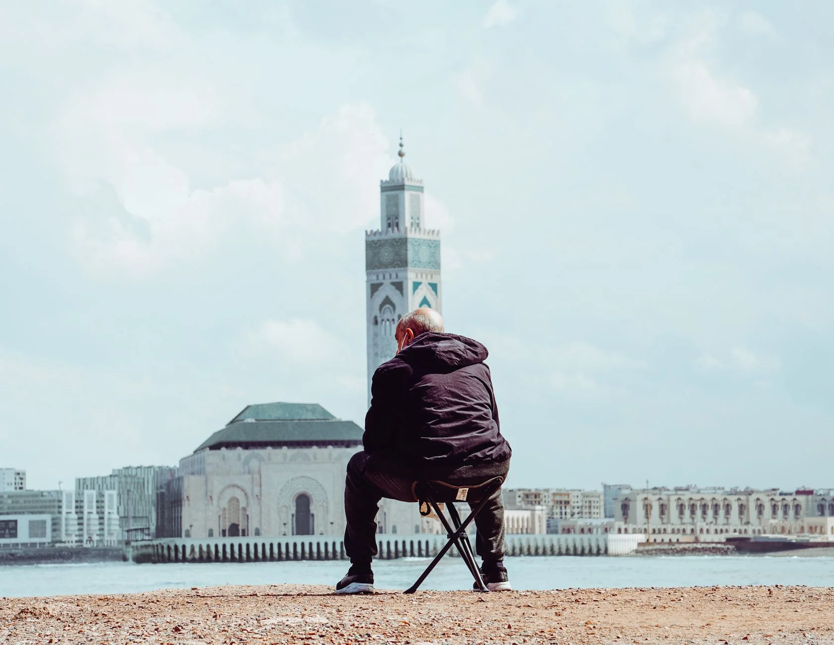 A seated man looking across the Casablanca waterfront towards Hassan II Mosque