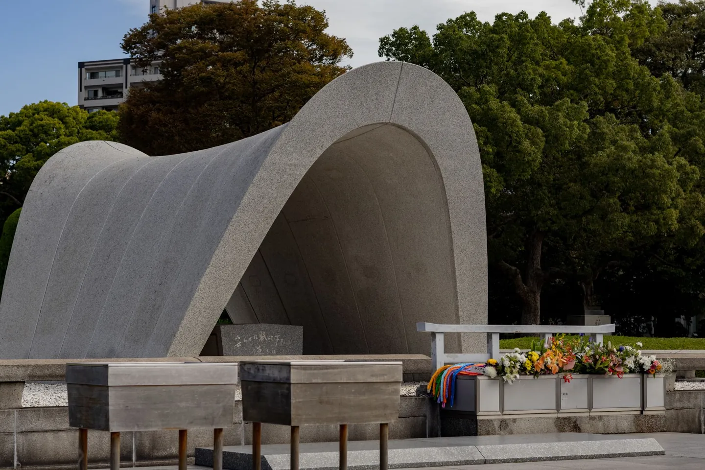 The curved Memorial Cenotaph in Hiroshima Peace Memorial Park with flowers and paper cranes