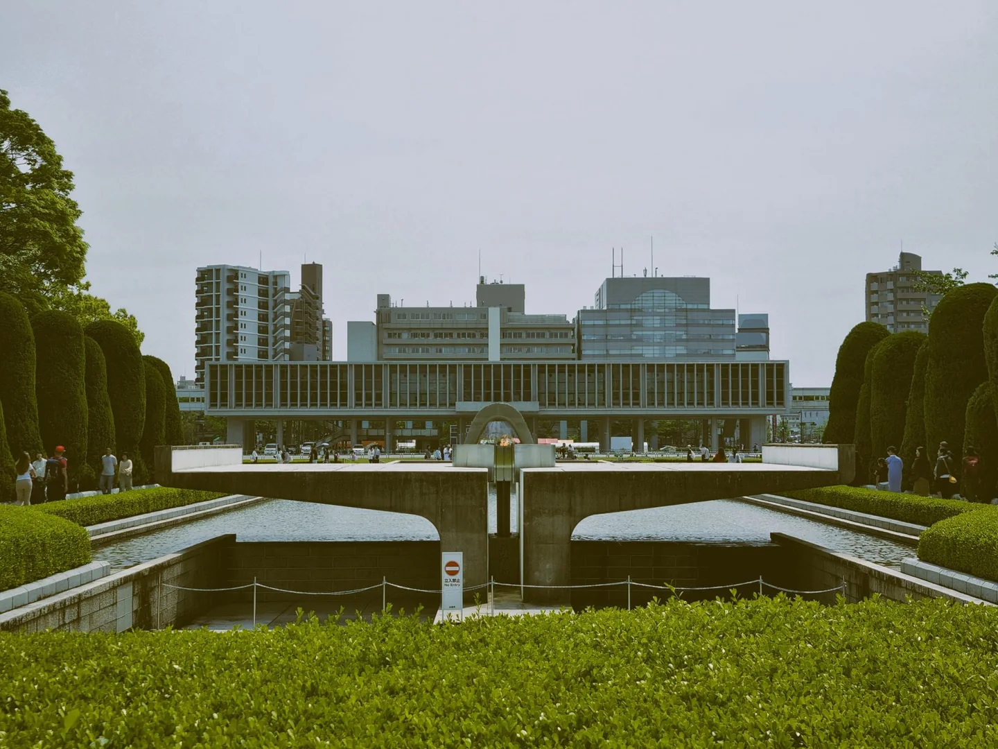 Hiroshima Peace Memorial Museum’s raised main building beyond the Flame of Peace and cenotaph
