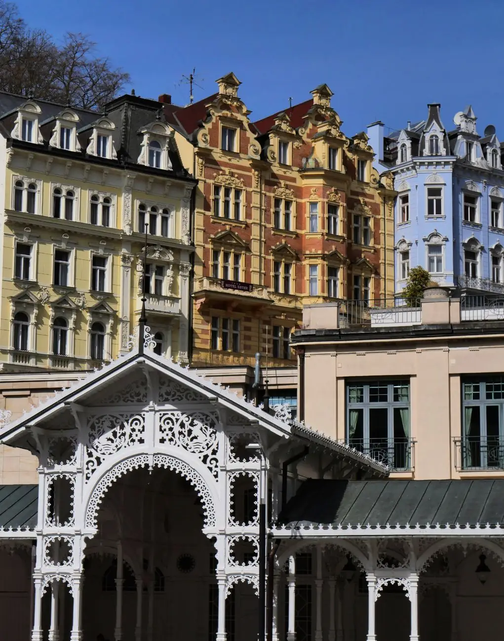 Carved white Market Colonnade woodwork beneath Karlovy Vary’s ornate town façades