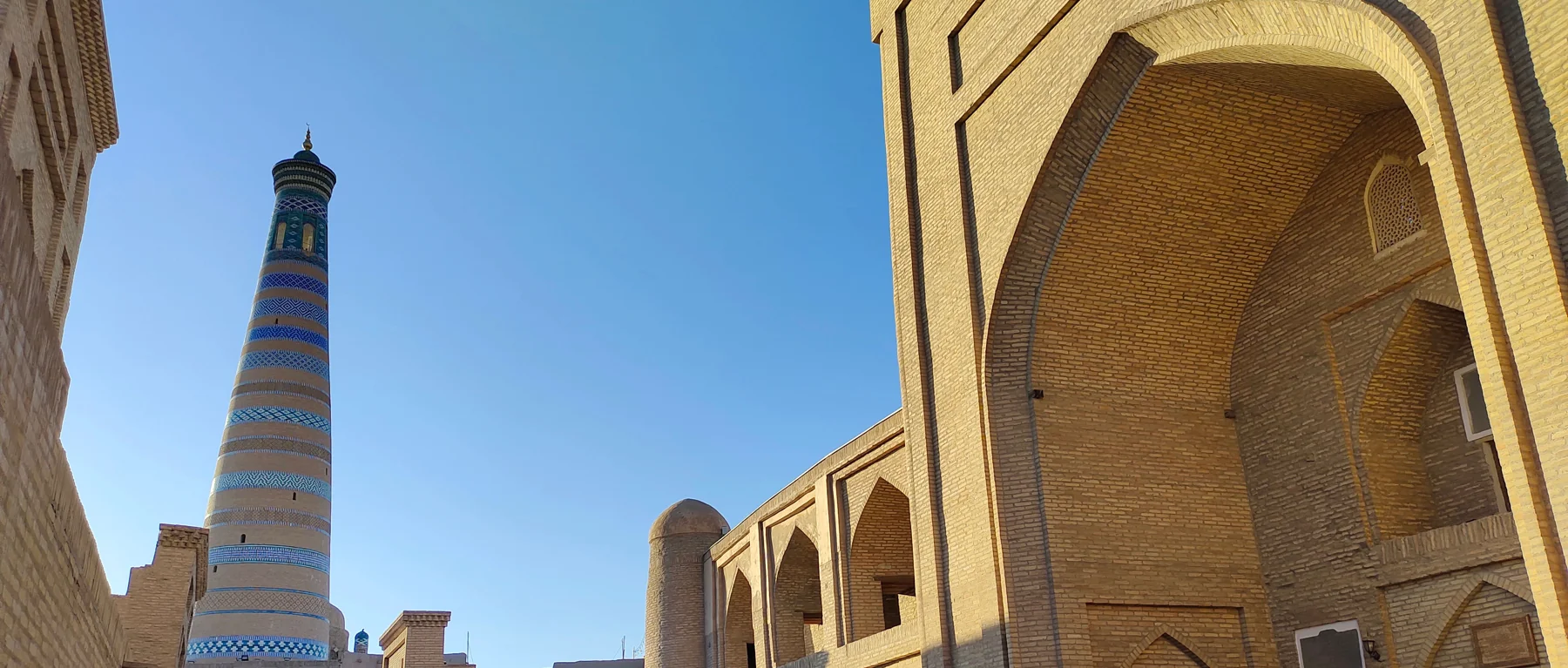 The banded Islam Khoja Minaret framed by brick architecture in Khiva