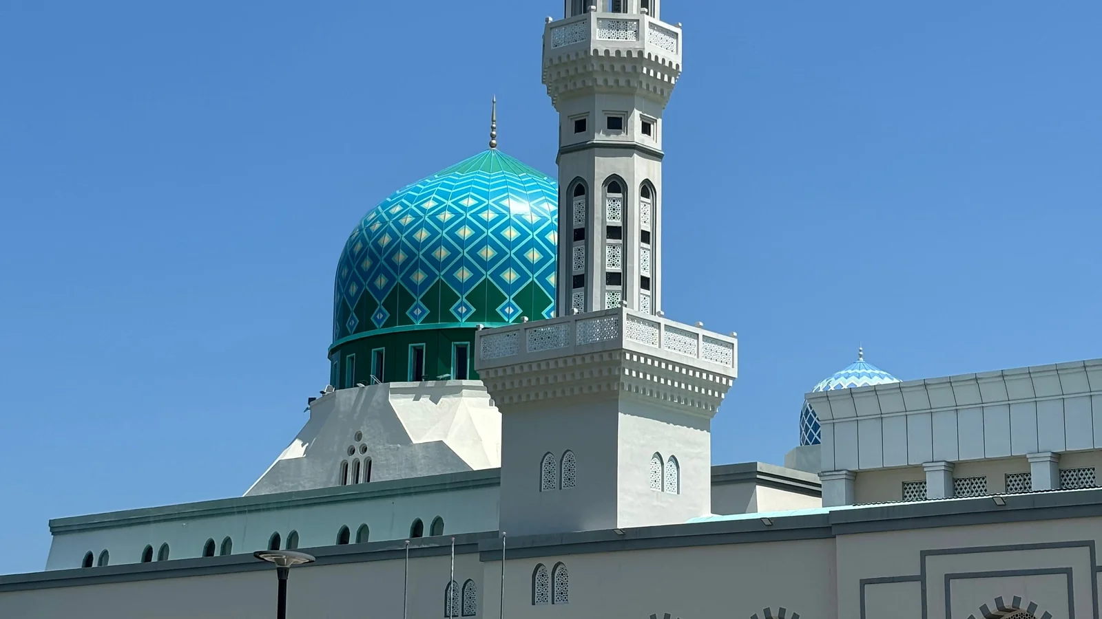 Detail of Kota Kinabalu City Mosque’s turquoise patterned dome and cream minaret against blue sky.