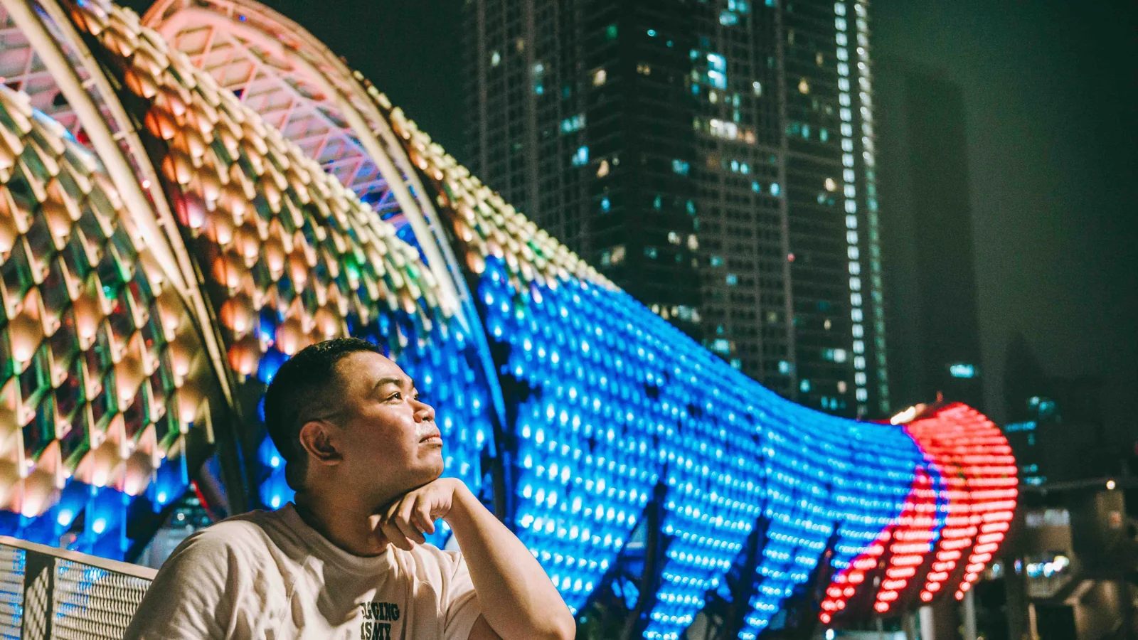 A visitor beside the colourful illuminated canopy of Saloma Link in Kuala Lumpur at night.