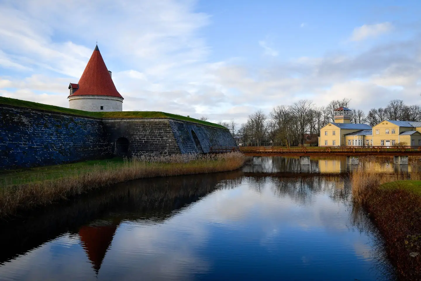 Kuressaare’s outer fortification tower and stone wall reflected in the moat, with town buildings beyond