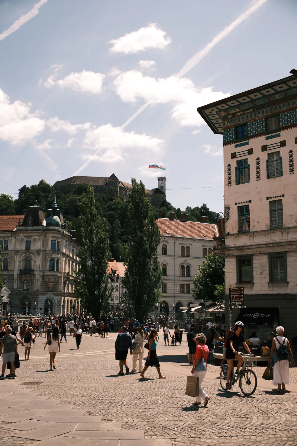 People crossing Prešeren Square with Ljubljana Castle rising behind