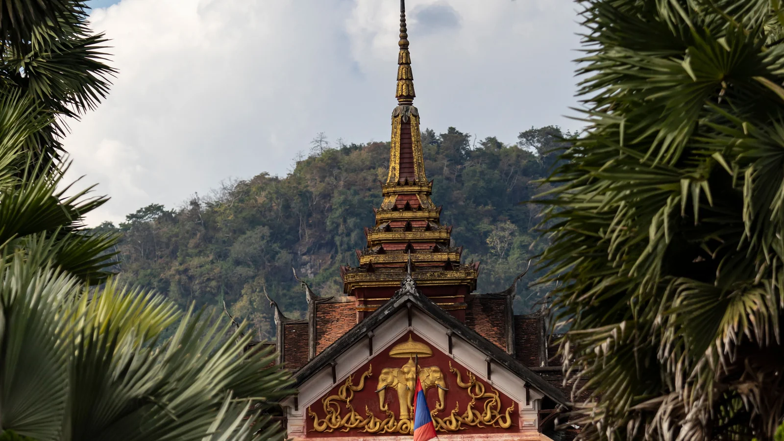 The National Museum’s central spire and decorated facade framed by palms in Luang Prabang.
