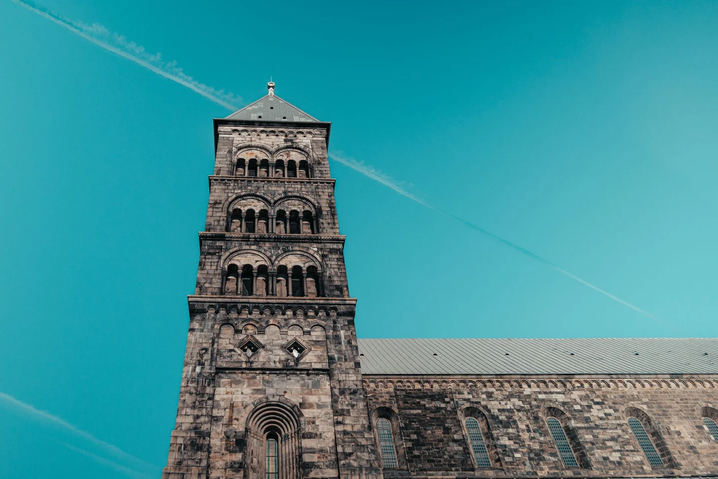 A Romanesque tower and stone arches of Lund Cathedral against a blue sky
