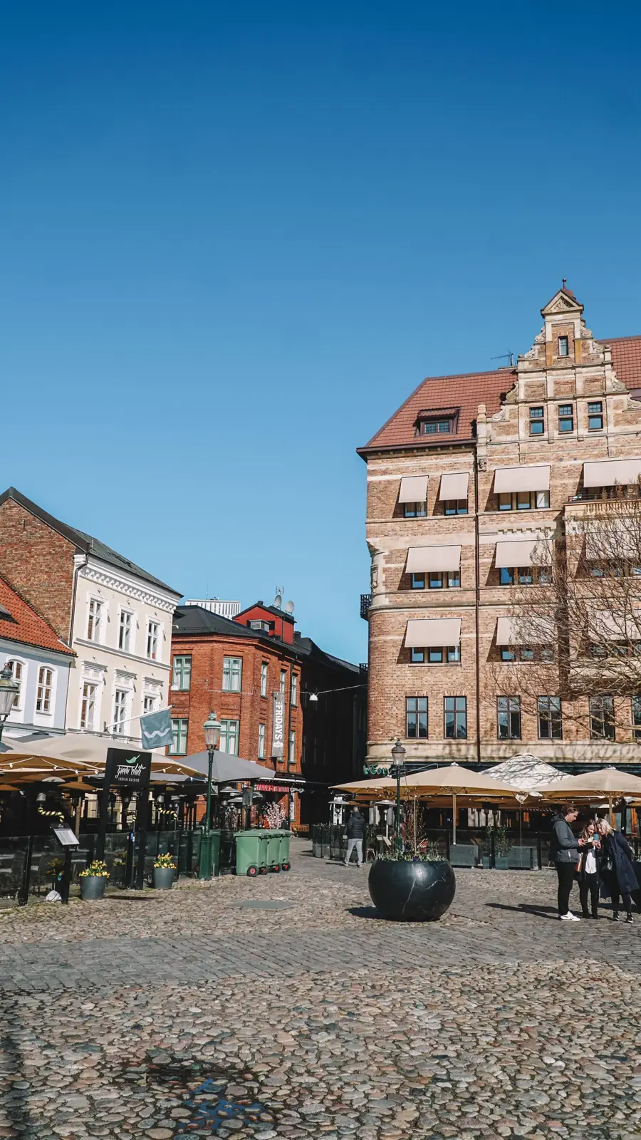 Historic brick buildings and outdoor tables at Malmö’s cobbled Lilla Torg