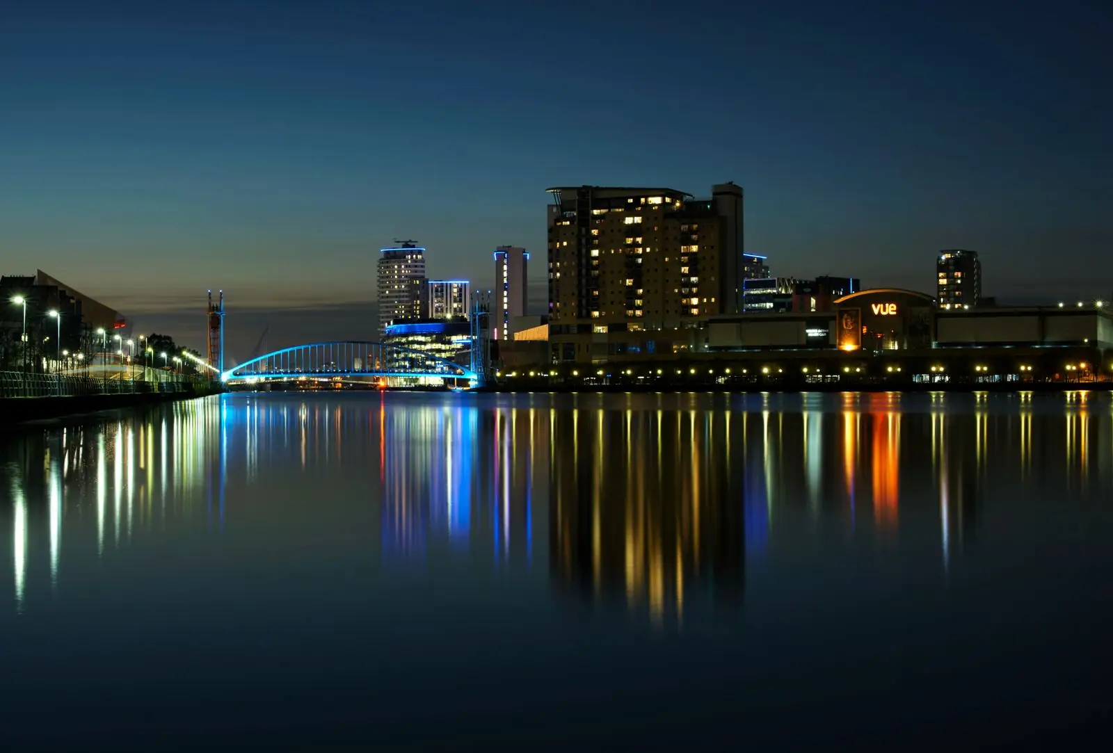 Illuminated buildings and footbridge reflected in the water at Salford Quays