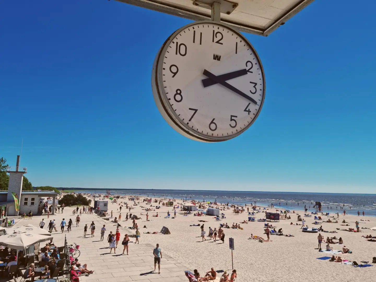 A clock above a summer view of the crowded sand and sea at Pärnu Beach