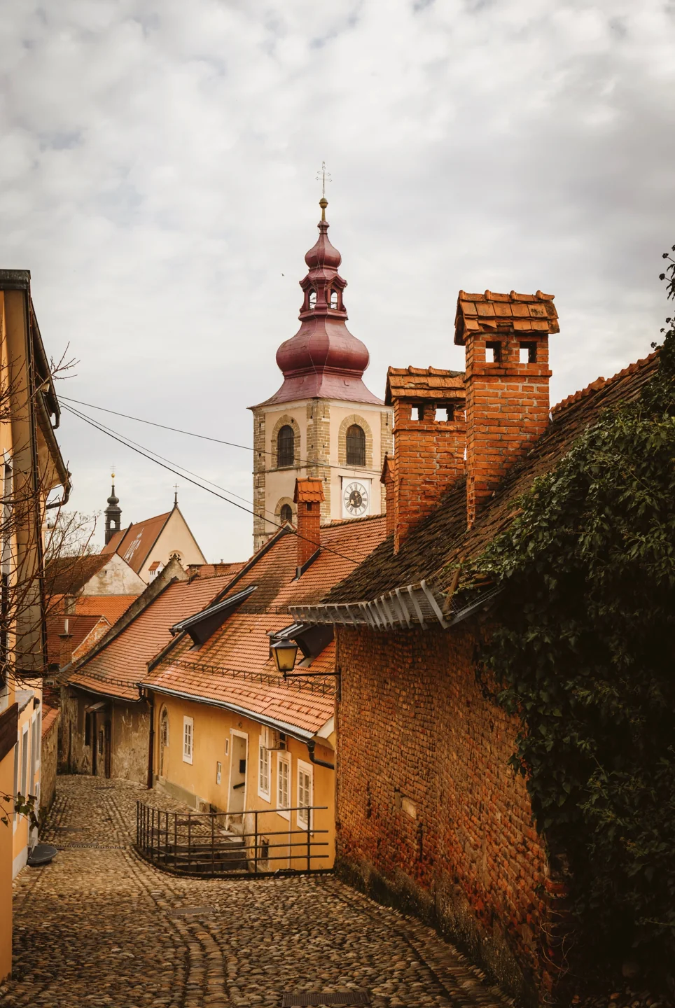 A cobbled old-town lane in Ptuj with the City Tower rising beyond