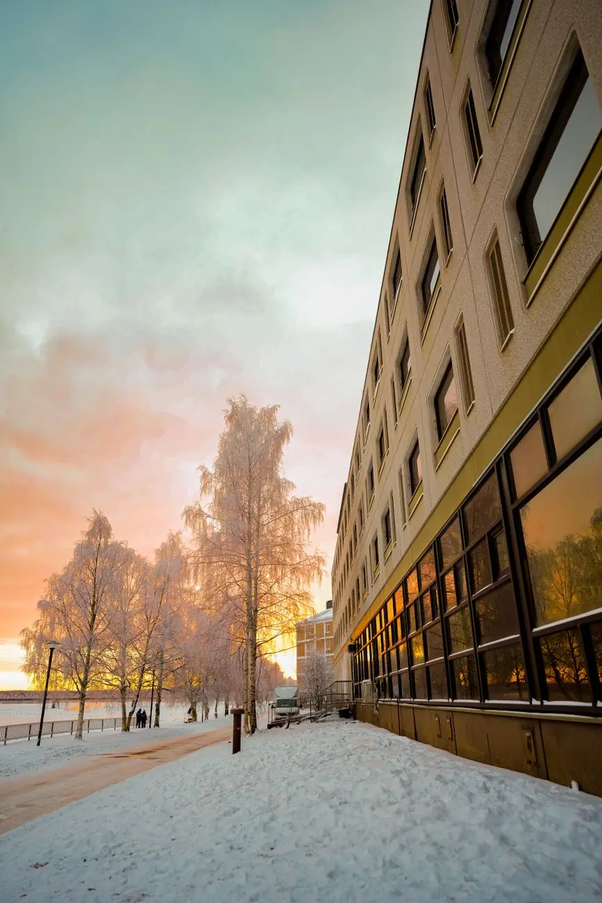 Snow-covered central Rovaniemi riverbank beside a building, with the Ounaskoski bridge in the distance