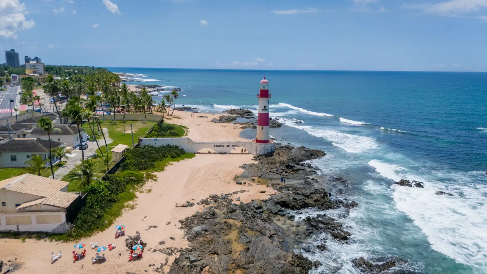 Red-and-white Farol de Itapuã beside its sandy beach and rocky shore