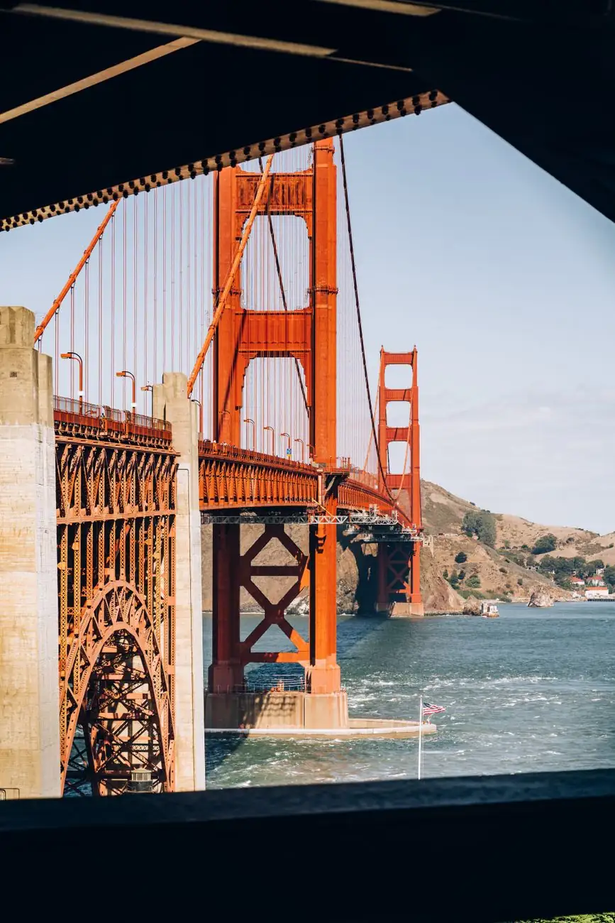The Golden Gate Bridge’s orange suspension towers viewed beneath a structural arch near its south end