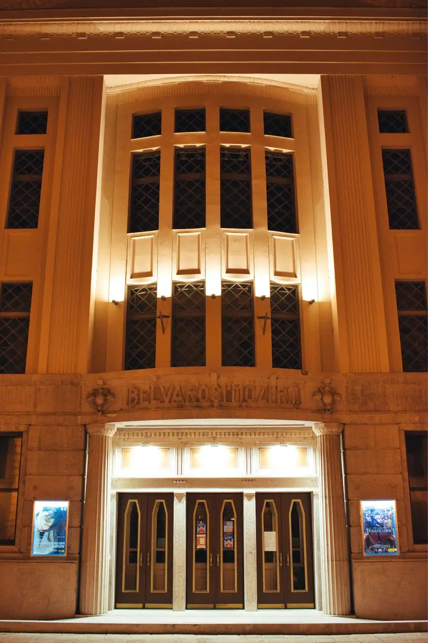 Belvárosi Mozi’s illuminated entrance in Szeged with film posters beside the doors