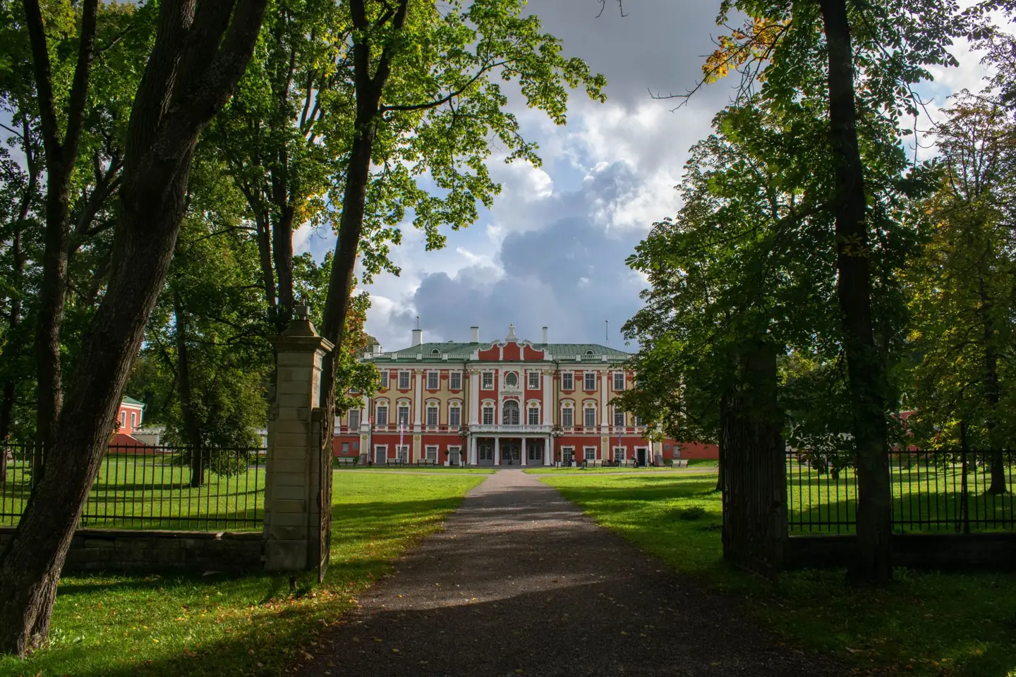 Kadriorg Palace’s red-and-white Baroque façade beyond a path and lawn framed by trees in Tallinn