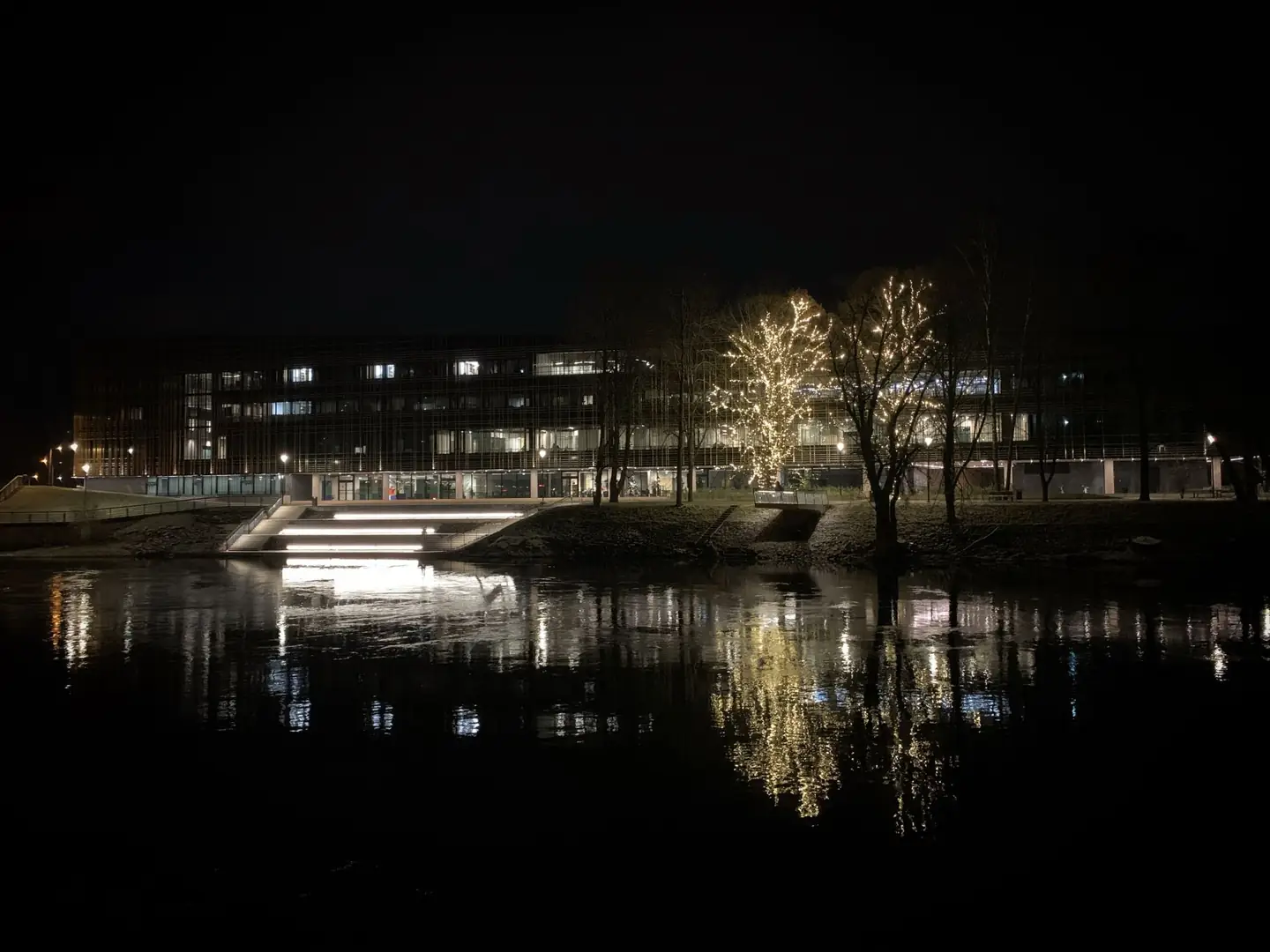 The University of Tartu Delta Centre and illuminated riverside steps reflected in the Emajõgi at night