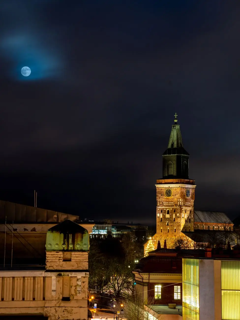 Turku Cathedral illuminated beneath the moon, viewed across central rooftops