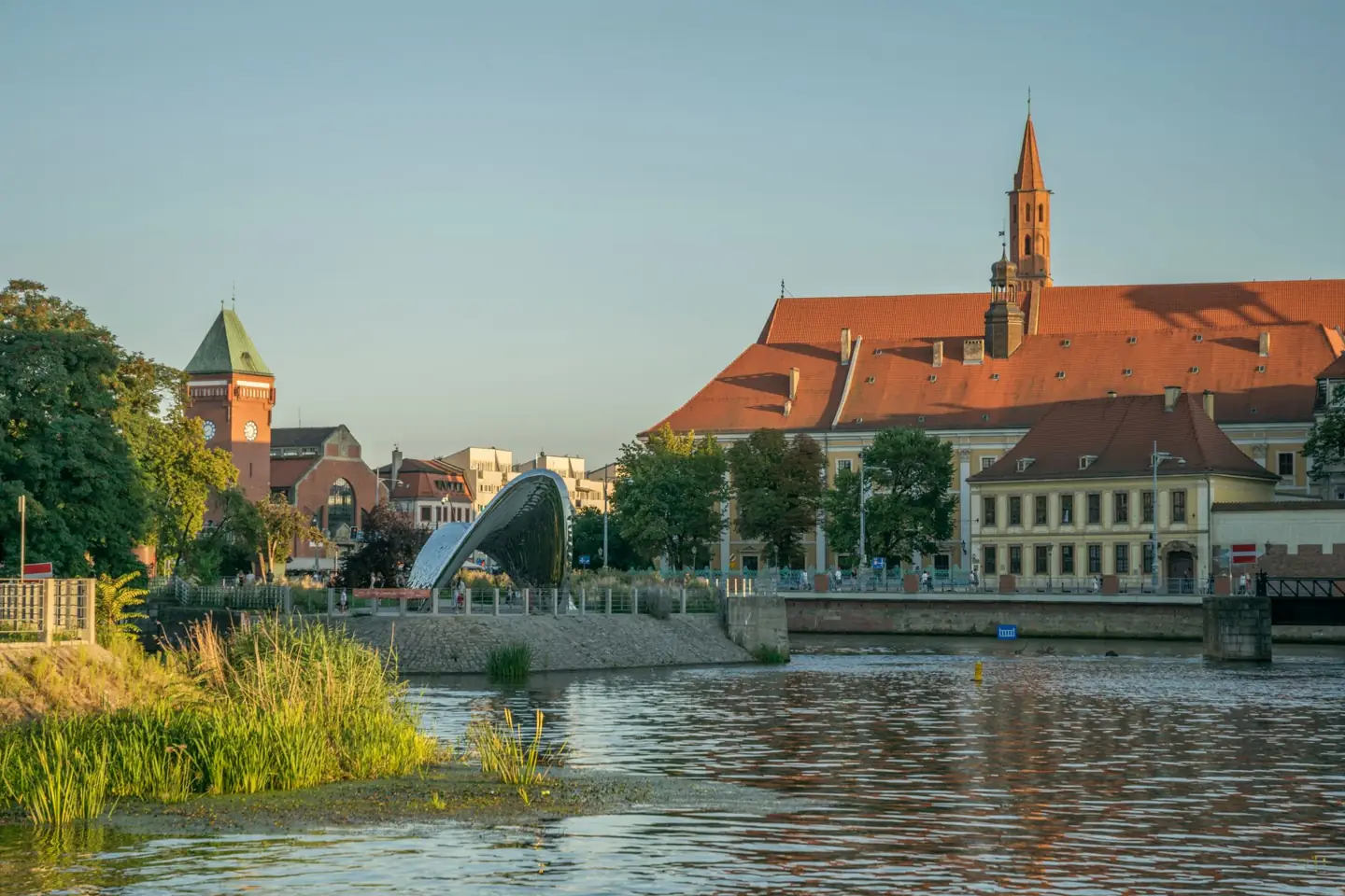 An arched pedestrian bridge and historic roofs beside Wrocław’s central Odra islands in evening light