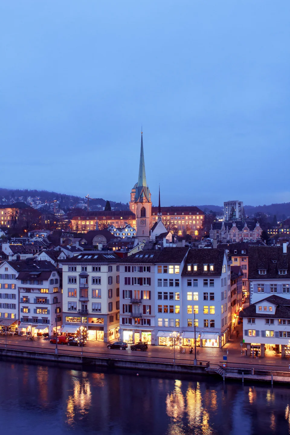 Illuminated old-town buildings and St Peter’s clock tower beside Zürich’s Limmat at dusk