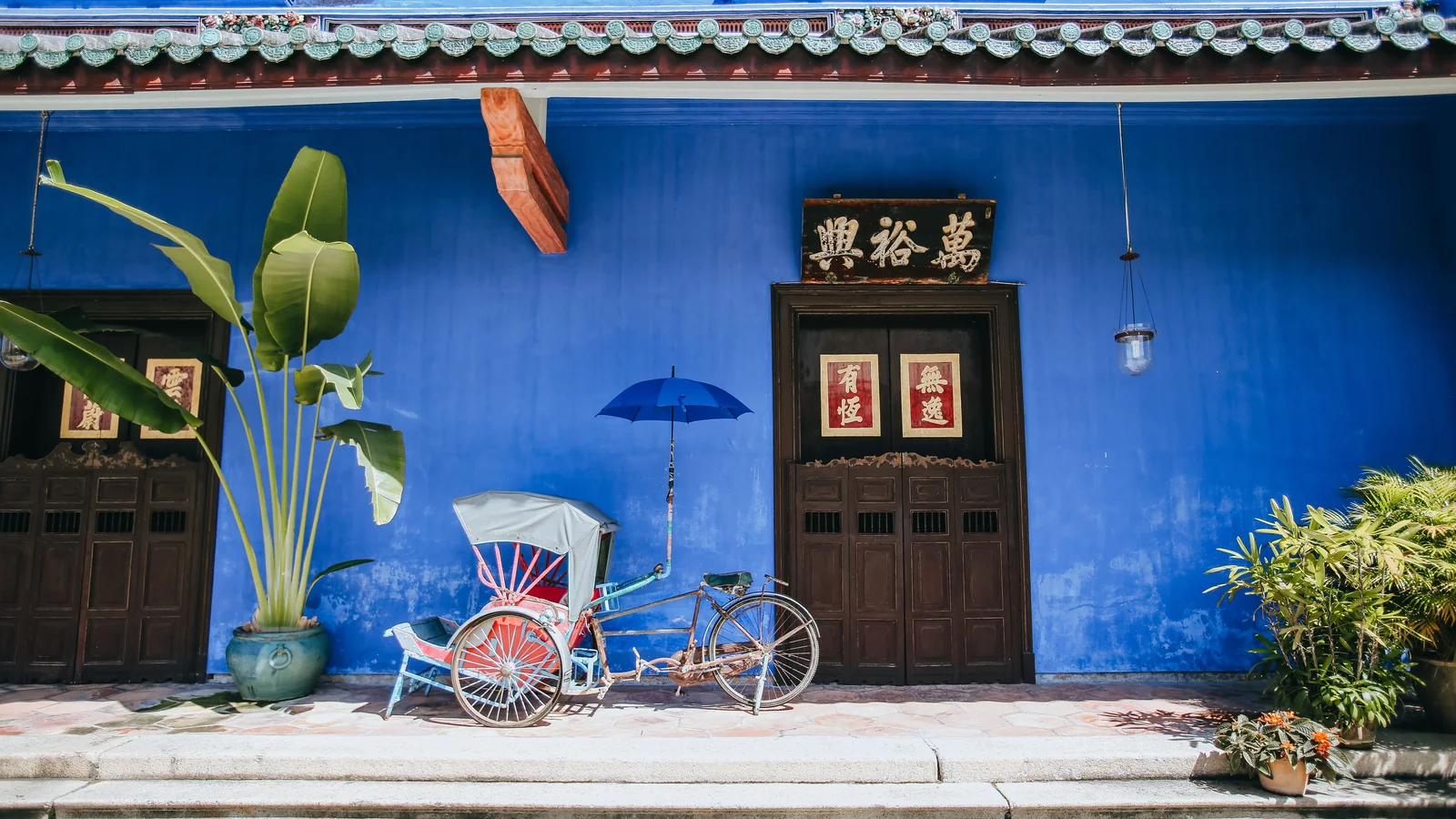 A trishaw outside Cheong Fatt Tze Mansion’s indigo facade and inscribed doors in George Town.