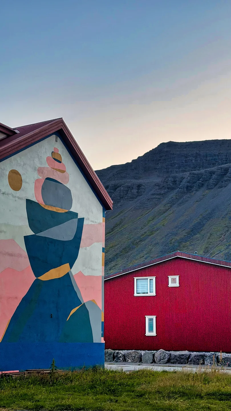 A colourful geometric mural on a gabled building with Ísafjörður’s mountain slopes behind