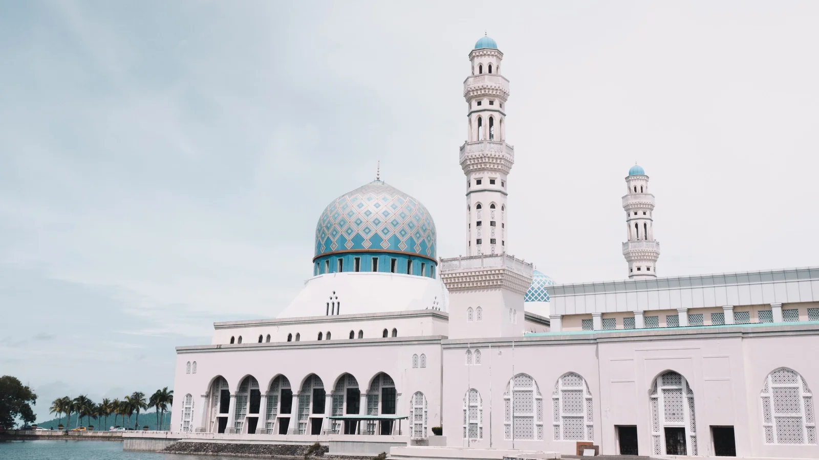 Kota Kinabalu City Mosque with patterned dome and minarets beside its lagoon.