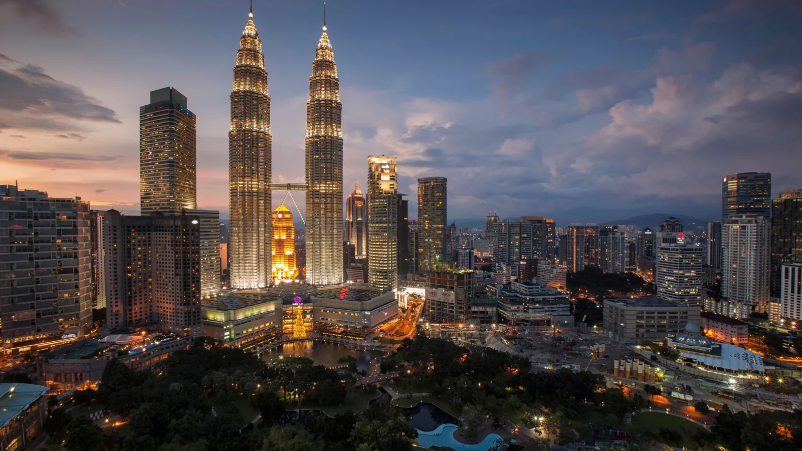 The illuminated Petronas Twin Towers above KLCC Park and Kuala Lumpur’s skyline at dusk.