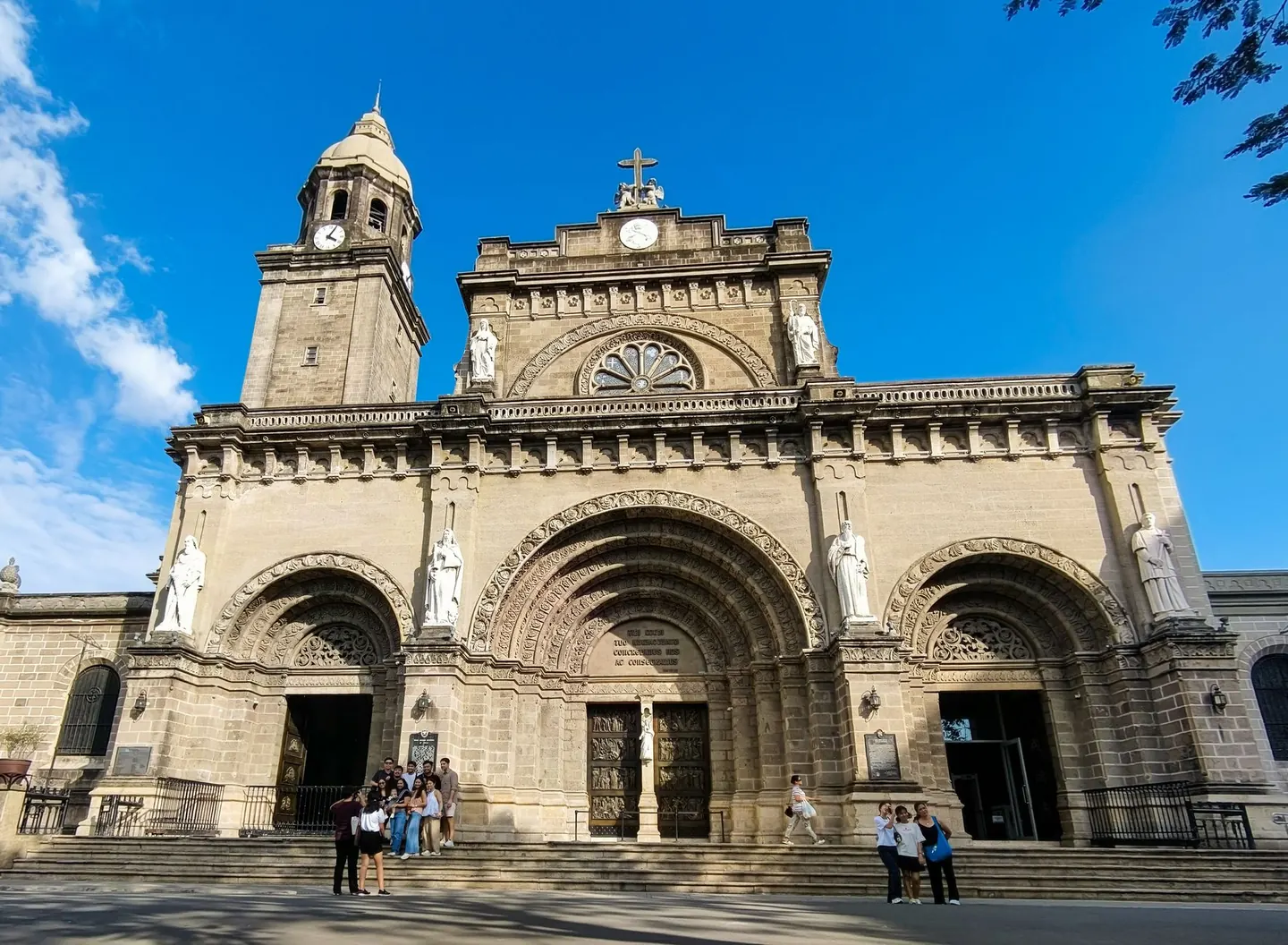 Manila Cathedral’s three-arched stone facade and bell tower beneath a blue sky
