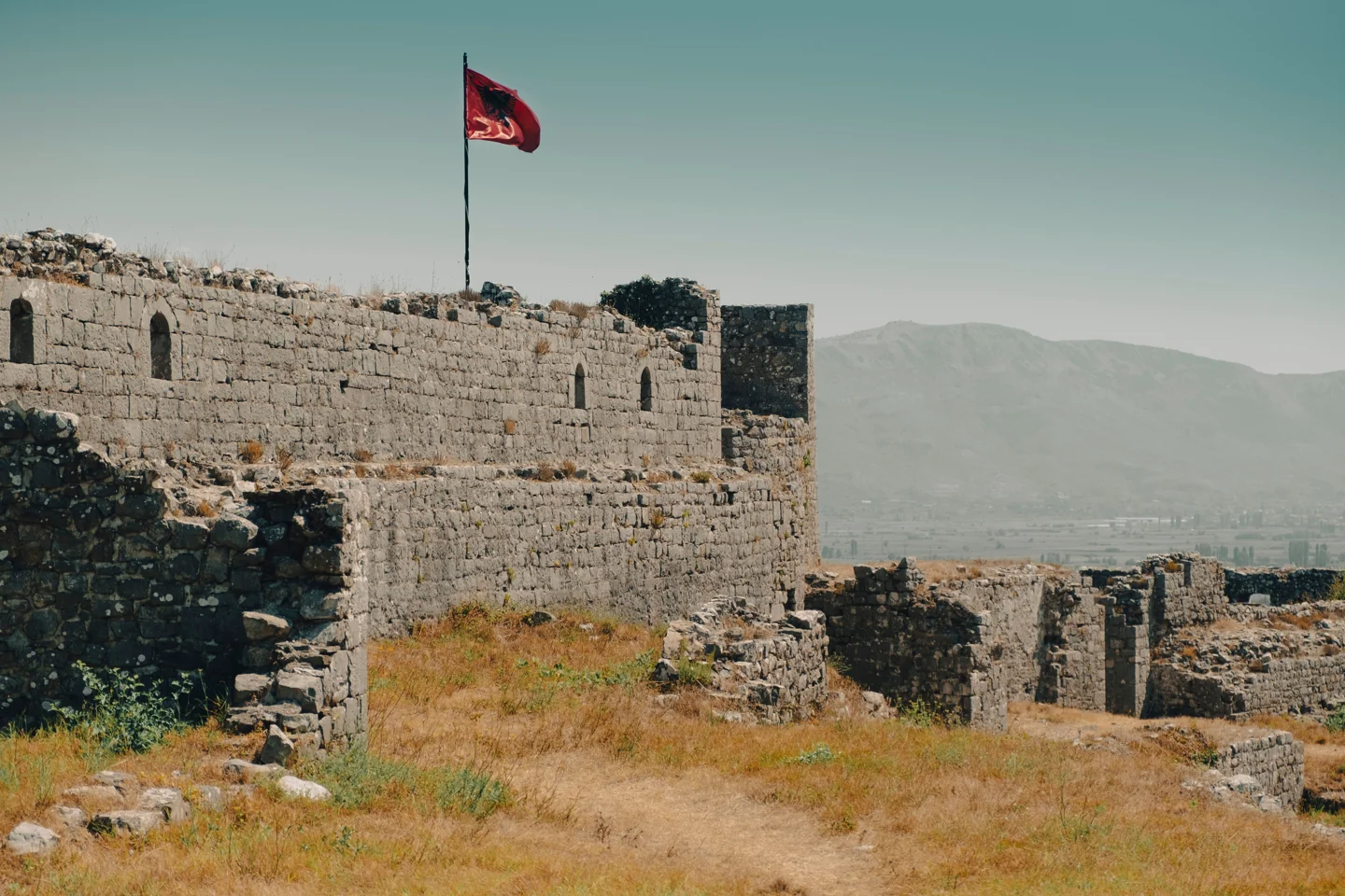 Stone walls and towers of Rozafa Castle in Shkodër with the Albanian flag and distant mountains
