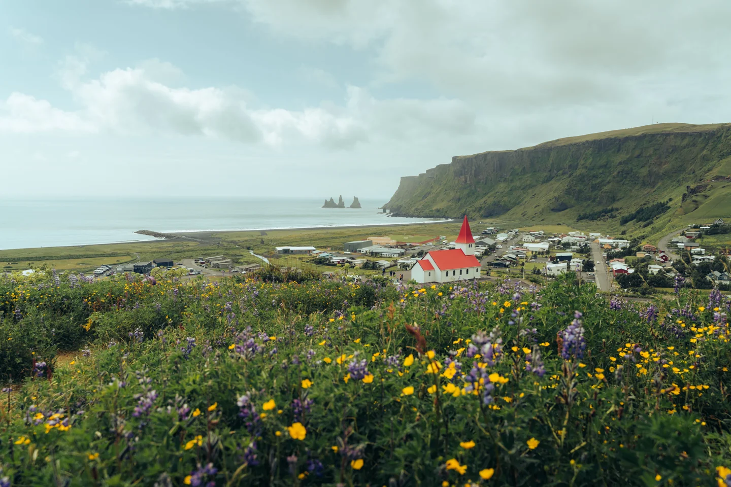 Vík village and its red-roofed church above the coast, with Reynisdrangar sea stacks beyond