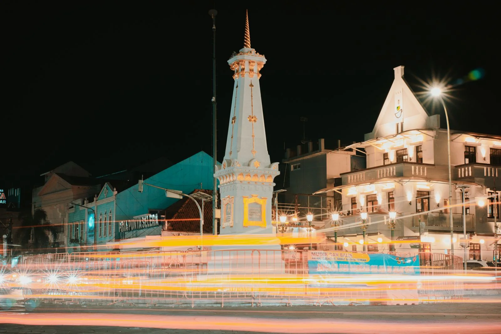 Tugu Yogyakarta rises above bright traffic trails at a city intersection after dark